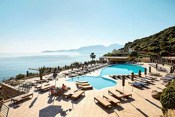 Hotellpool med solstolar och utsikt över havet och berg. (AI-genererad text)