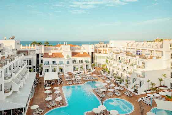 Vy över hotellområde med pool och solstolar, havet syns i bakgrunden. (AI-genererad text)