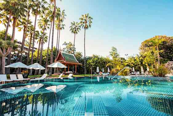 En swimmingpool omgiven av solstolar, parasoller och palmer med ett thailändskt paviljong i bakgrunden. (AI-genererad text)