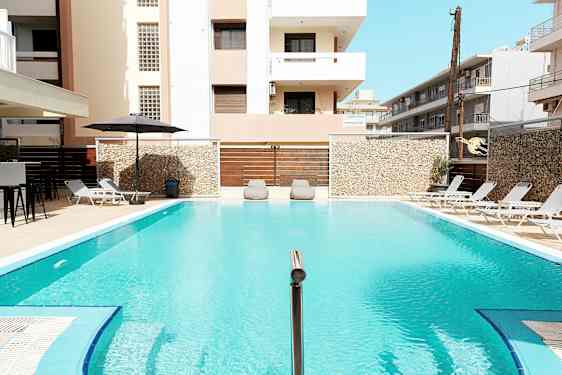 En utomhuspool omgiven av solstolar och byggnader. (AI-genererad text)