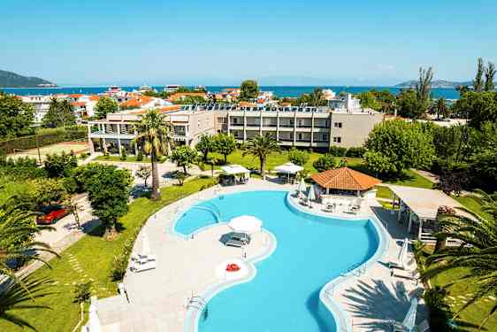 Hotellets utomhusområde med en stor pool, gröna trädgårdar och havet i bakgrunden. (AI-genererad text)