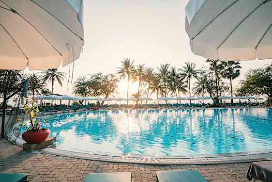 En solig dag vid en pool med parasoll och palmer i bakgrunden. (AI-genererad text)