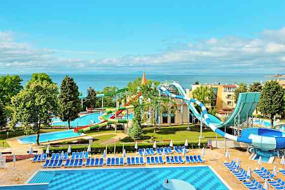 En vattenpark vid havet med vattenrutschbanor och pooler omgivna av solstolar och parasoller. (AI-genererad text)