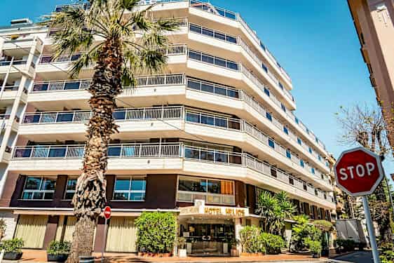 Ett hotell med flera våningar och en palmträd framför. Skylten "STOP" syns till höger. (AI-genererad text)