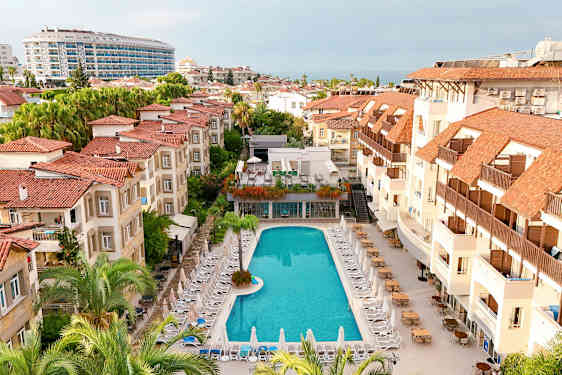 Hotellområde med en pool omgiven av solstolar och byggnader med röda tak. (AI-genererad text)