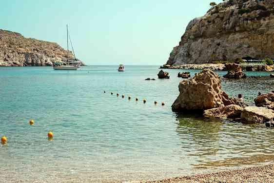 En vik med klara vattnet och steniga kust, där en båt och en mindre flytande farkoster syns i bakgrunden. (AI-genererad text)