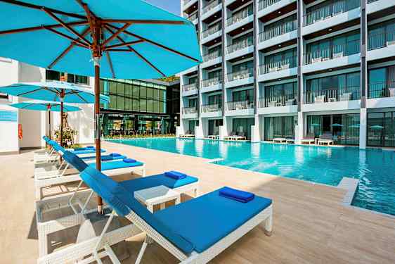 En swimmingpool på ett hotell med solstolar och parasoller i förgrunden. (AI-genererad text)