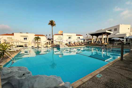 En utomhuspool framför vita byggnader med röda tak. (AI-genererad text)