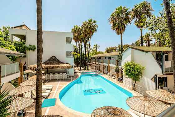 Utomhuspool omgiven av vita byggnader och palmer. (AI-genererad text)