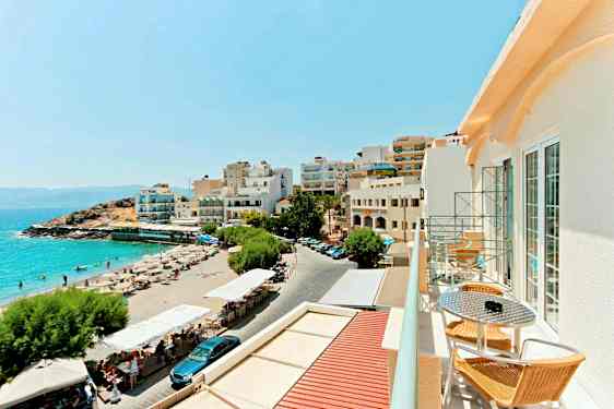 Utsikt över en sandstrand med solstolar och parasoller bredvid byggnader med utsikt över havet. (AI-genererad text)