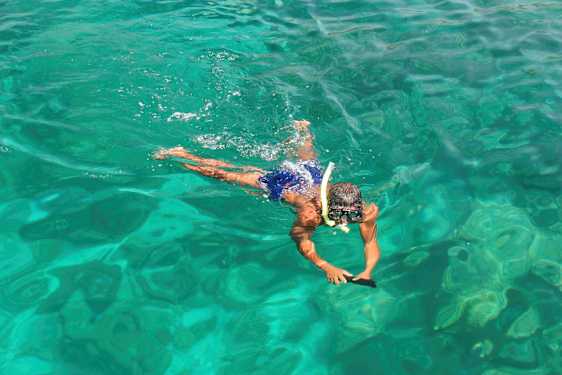 En person simmar i klart vatten med snorkelutrustning. (AI-genererad text)