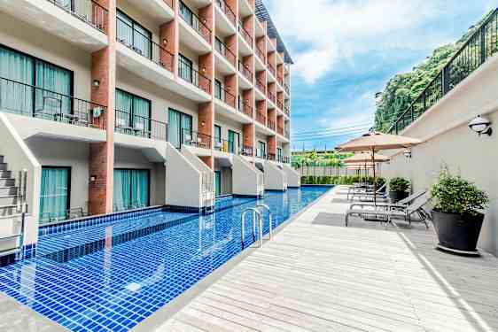 Ett hotell med flera våningar och en lång pool framför byggnaden, omgiven av solstolar och parasoller. (AI-genererad text)