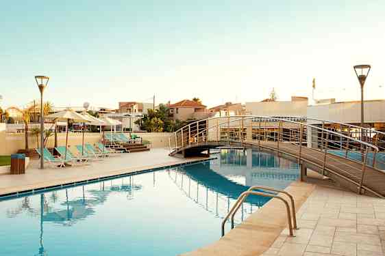 En utomhuspool med solstolar och en gångbro över vattnet. (AI-genererad text)