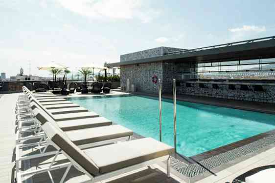 Bild av en solig takterrass med en pool omgiven av solstolar och parasoll. (AI-genererad text)