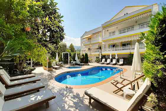 En solig hotellträdgård med en pool och solstolar. (AI-genererad text)