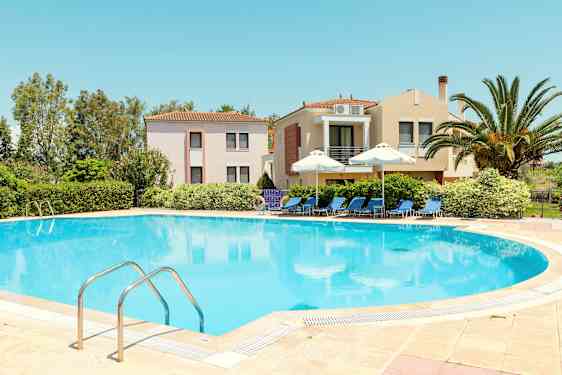 En pool omgiven av solstolar och parasoller, med byggnader och grönska i bakgrunden. (AI-genererad text)