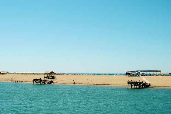 En strand vid havet med solstolar och parasoller samt en träbrygga. (AI-genererad text)