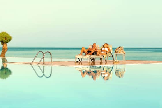 Två personer ligger på solstolar vid en pool med utsikt över havet. (AI-genererad text)