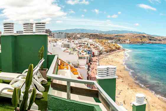 Vy från en takterrass med solstolar mot en strand och stadsmiljö. (AI-genererad text)