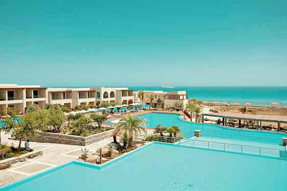 En semesterresort med poolområde, omgärdat av tropiska växter och byggnader samt med utsikt över havet. (AI-genererad text)