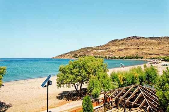 En strand med klart blått hav, omgivande grönska och en trästruktur i förgrunden. (AI-genererad text)