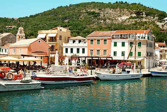 En hamn med flera båtar framför färgglada byggnader och omgiven av kullar. (AI-genererad text)