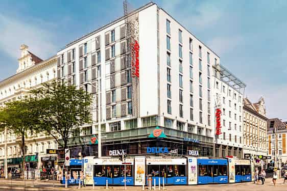 En flerfärgad spårvagn framför ett modernt hotell i stadslandskap. (AI-genererad text)