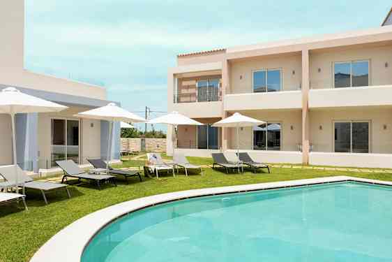 Poolområde med solstolar och parasoller framför ljusa byggnader. (AI-genererad text)