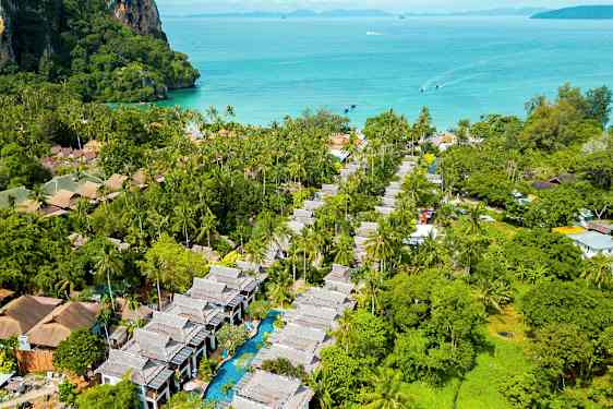 Flygbild över ett tropiskt område med palmer, byggnader och en pool, med havet i bakgrunden. (AI-genererad text)