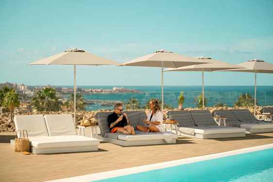 Solstolar och parasoller vid en pool med utsikt över havet. (AI-genererad text)