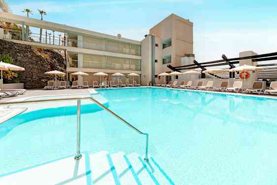 En pool med klarblått vatten omgiven av solstolar och parasoll. (AI-genererad text)