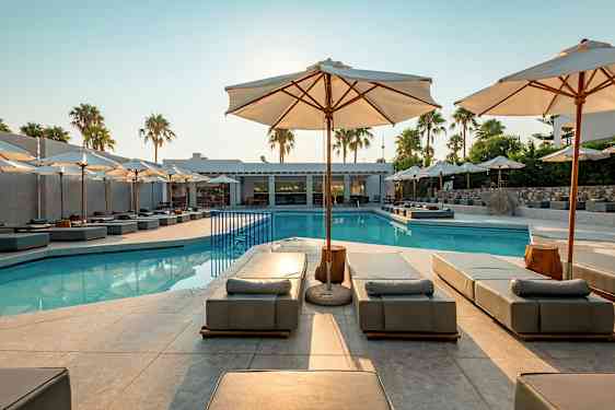 Utomhuspool med solbäddar och parasoller, omgiven av palmer och byggnader. (AI-genererad text)