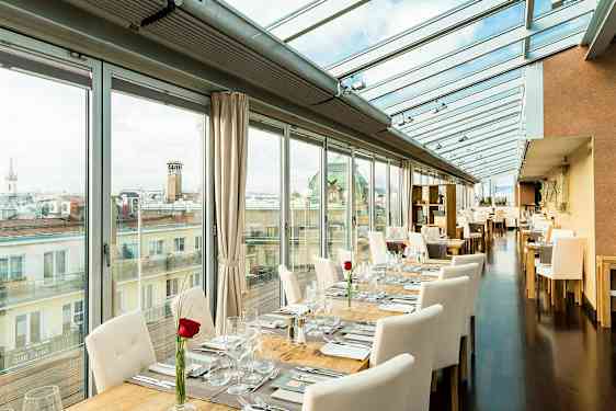 En ljus restaurang med glasväggar och tak, borden är dukade med vita stolar och en ros på varje bord. (AI-genererad text)