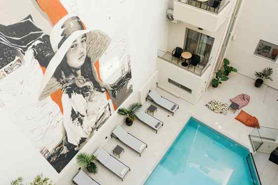 Bild av en pool omgiven av solstolar och sittsäckar, med en stor väggmålning. (AI-genererad text)