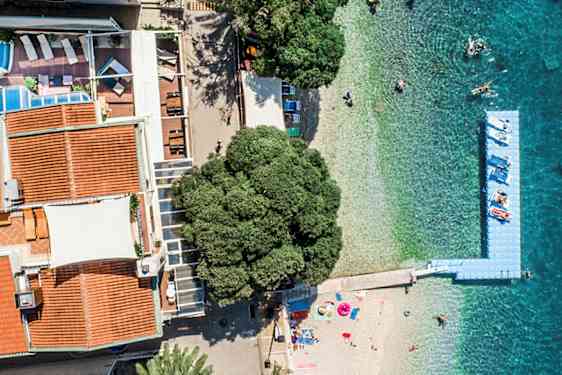 Flygbild av byggnader med röda tak, en pool, en strand och turkosblått hav. (AI-genererad text)