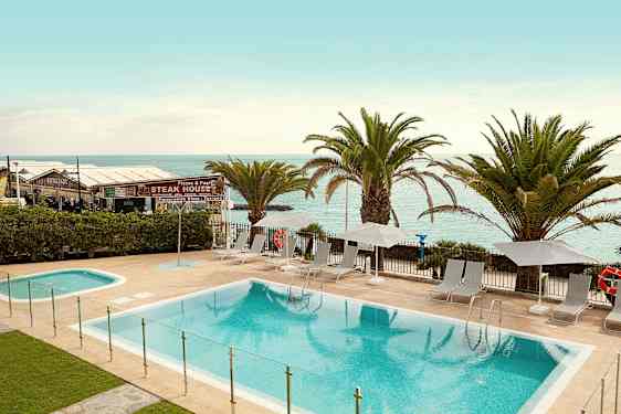 Poolområde med solstolar och parasoller vid stranden. (AI-genererad text)