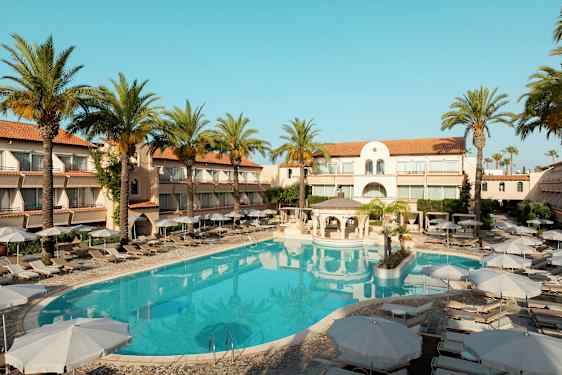 Hotellbyggnad med solstolar och parasoller kring en utomhuspool, omgivna av palmer. (AI-genererad text)