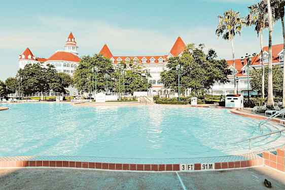 Bild av en pool med ett elegant vitt hotell med röda tak i bakgrunden. (AI-genererad text)