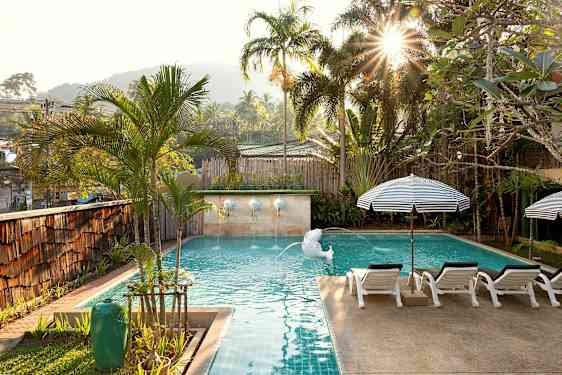 En solbelyst pool omgiven av palmer och solstolar. (AI-genererad text)