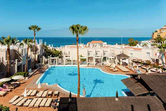 Vy över ett hotellområde med pool och solstolar, havet synligt i bakgrunden. (AI-genererad text)