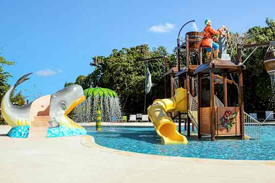 En barnpool med vattenrutschbanor, ett piratskeppstema och figurer som en val och en palm. (AI-genererad text)