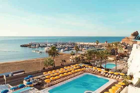 Vy över en pool och en strand med en hamn i bakgrunden. (AI-genererad text)