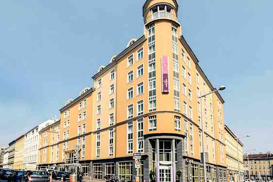 En ljusgul flerfaldigt fönstrad byggnad med skylt och rundad hörningsfasad. (AI-genererad text)