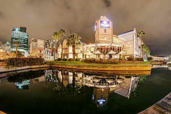 Hotell och byggnader vid en vattenkanal på natten med spegelreflektioner i vattnet. (AI-genererad text)