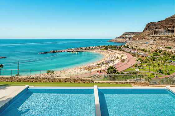 Bild av en strand med parasoller, turkost vatten och en pool i förgrunden. (AI-genererad text)