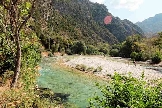 En flod med klart vatten som flyter genom ett grönskande landskap med berg i bakgrunden. (AI-genererad text)