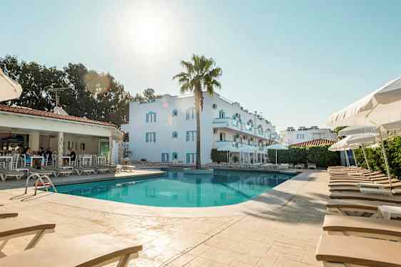 Bild av en pool med solstolar och parasoller, bakom ses en vit byggnad och ett öppet reservationsområde. (AI-genererad text)