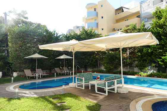 Utomhuspool med solstolar och parasoller, omgiven av träd och byggnader. (AI-genererad text)