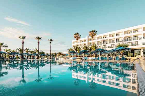 Exteriör av ett hotell med en stor pool framför och omgivande palmer. (AI-genererad text)