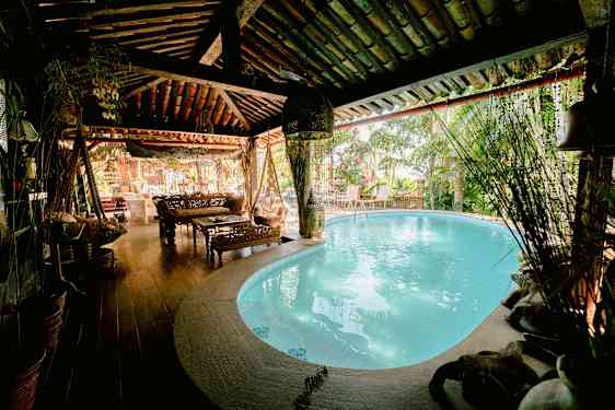 Ett mysigt utrymme med en pool inomhus, möbler i trä och växter runtom. (AI-genererad text)